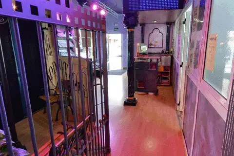 Pasillo de Inkaddiction en Valladolid, con una reja de forja a la izquierda, suelo de madera y el mostrador al fondo bajo luces moradas